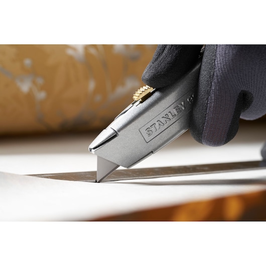 Photo of STANLEY 0-11-911 utility knife cutting paper held by a gloved hand.