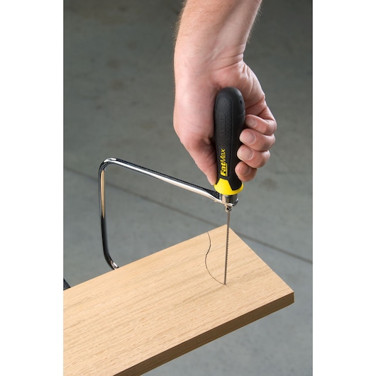 STANLEY 0-15-106 coping saw with black and yellow handle cutting a curved line in a wooden board, close-up.