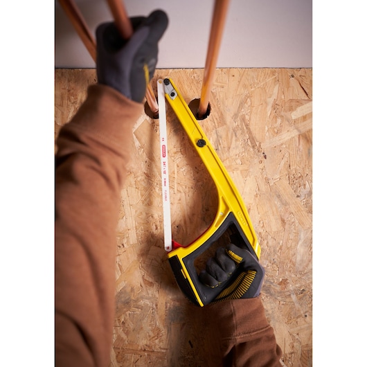 STANLEY 0-20-108 hacksaw with yellow frame cutting copper pipe, viewed from above, held by gloved hands.