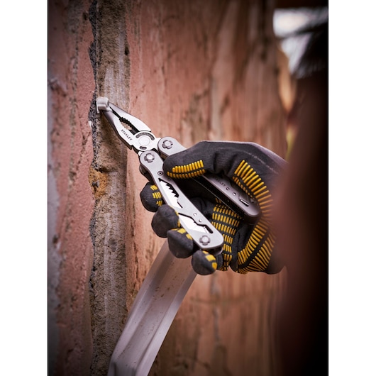 STANLEY 0-84-519 multi-tool pliers used on a brick wall, close-up photography of gloved hand.