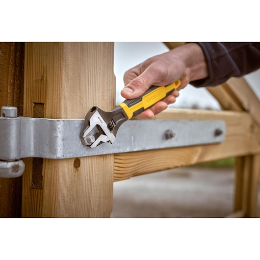 STANLEY 0-90-947 adjustable wrench used on metal bolt, close-up photo, hand-held tool on wooden gate.