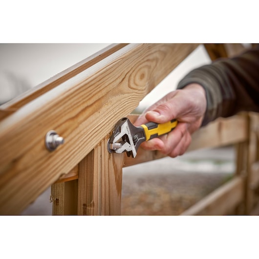 Photo of STANLEY 0-90-948 adjustable wrench tightening bolt on wooden fence outdoors.