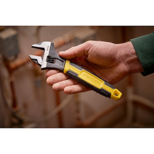 STANLEY 0-90-949 adjustable wrench with yellow and black handle, held in hand, plumbing background.