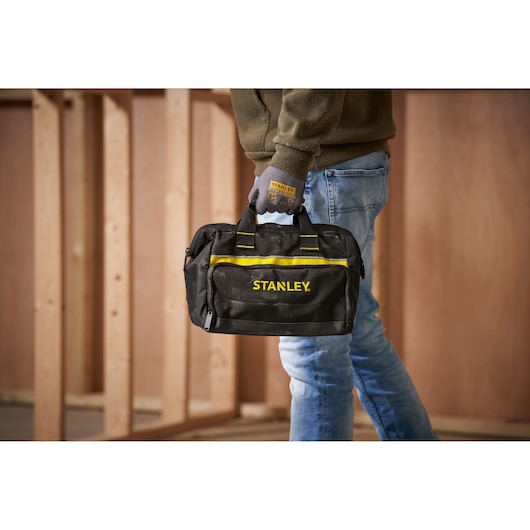 Stanley 1-93-330 tool bag with yellow accents held by person in work gloves, shown in workshop setting.