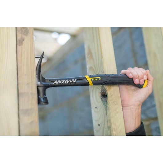 STANLEY FMHT1-51277 claw hammer in use, black handle, driving nail into wooden beams.