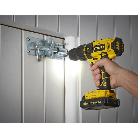 Photo of STANLEY SCH20S2K cordless drill driving a screw into a metal door latch, side view.