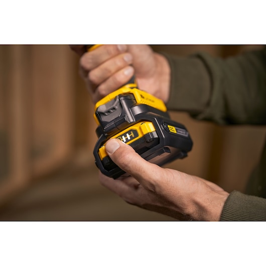 Close-up photo of a person attaching a STANLEY SFMCB100 black and yellow power tool battery.
