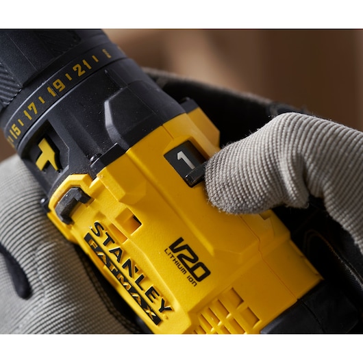 Photo of STANLEY SFMCD711B yellow cordless drill with V20 branding, gear switch held by gloved hand, close-up.