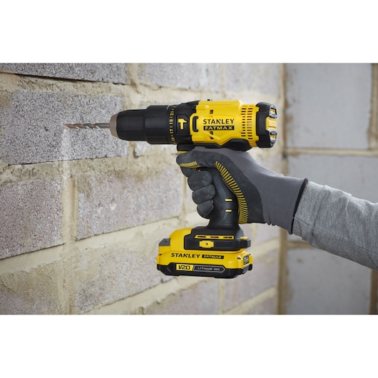 Stanley SFMCD711B yellow cordless drill in use on a brick wall, FATMAX branding visible.