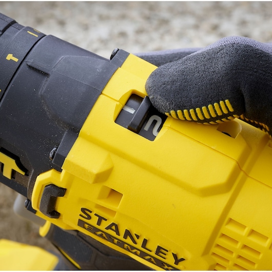 Photo of STANLEY SFMCD711B drill close-up showing speed selector being adjusted with gloved hand.