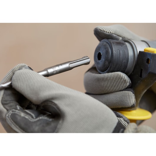 Photo of STANLEY SFMCH900B rotary hammer with gloved hands inserting a drill bit, close-up angle.