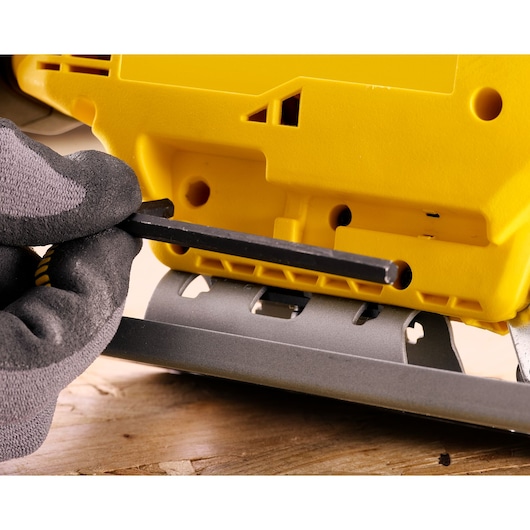 Gloved hand uses hex key to adjust yellow STANLEY tool on a wooden surface.
