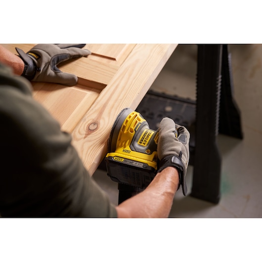 Photo of STANLEY SFMCW220B cordless sander being used on a wooden surface, close-up view.