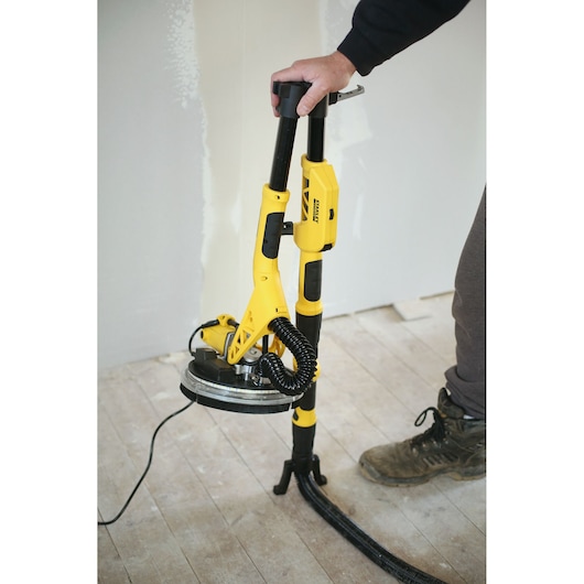 Photo of a STANLEY SFMEE500S drywall sander in use on a wooden floor, shown with handle and vacuum hose.