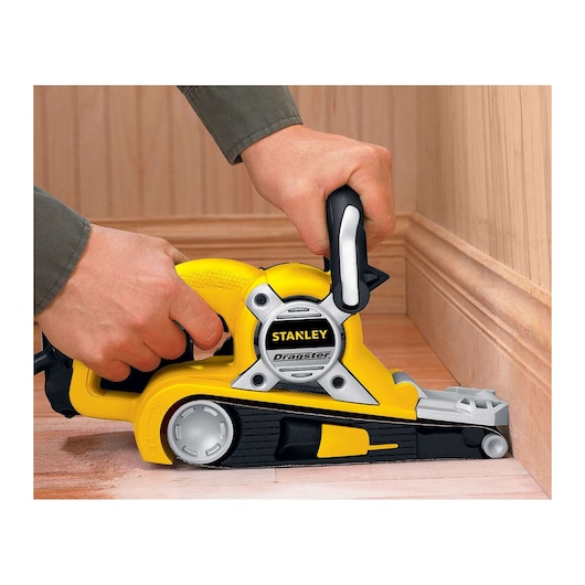 Stanley STBS720 belt sander being used on a wooden floor, close-up side angle, yellow and black design.