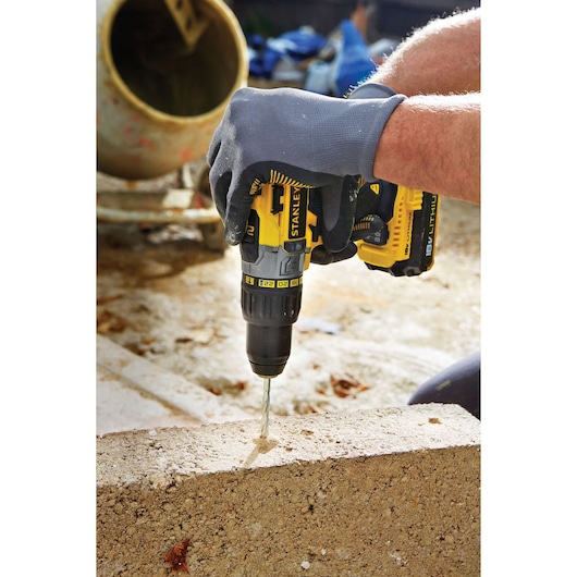 STANLEY STDC18LHBK cordless drill in use drilling into concrete block, construction site background.