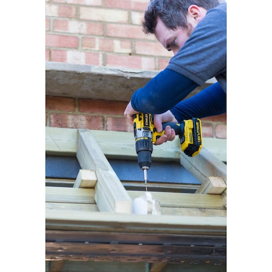 Photo of STANLEY STDC18LHBK cordless drill in use on wood construction, side angle.