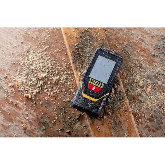 STANLEY STHT1-77140 laser distance measurer on dusty wooden surface, rugged and water-resistant design.