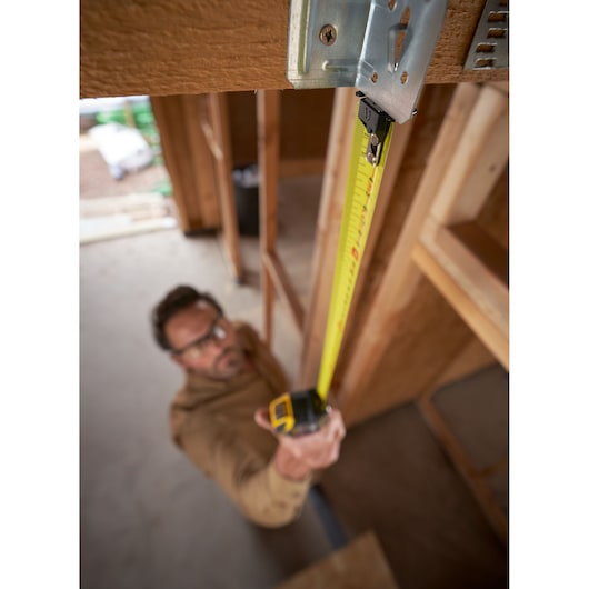 STANLEY XTHT0-33501 tape measure in use at construction site, vertical top-down angle.