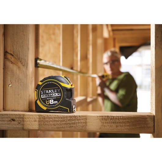 Photo of STANLEY FATMAX XTHT0-33501 8m tape measure on wooden frame at construction site.