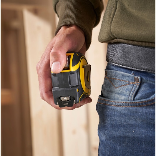 STANLEY XTHT0-33501 tape measure held in hand, close-up, next to jeans pocket, indoor setting.